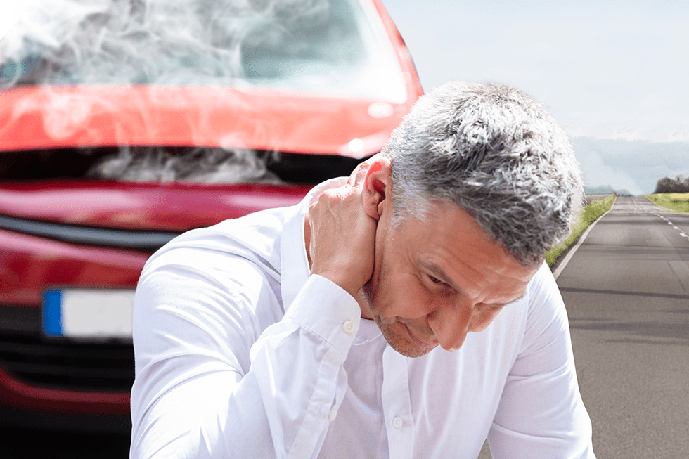 A man kneeling in front of a red crashed car holding his neck from a whiplash injury