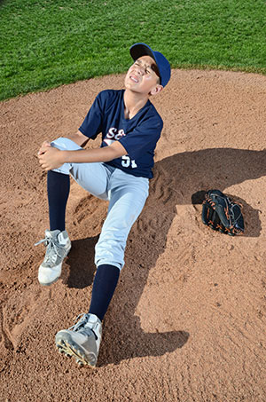 Little League pitcher on the mound holding knee in pain.